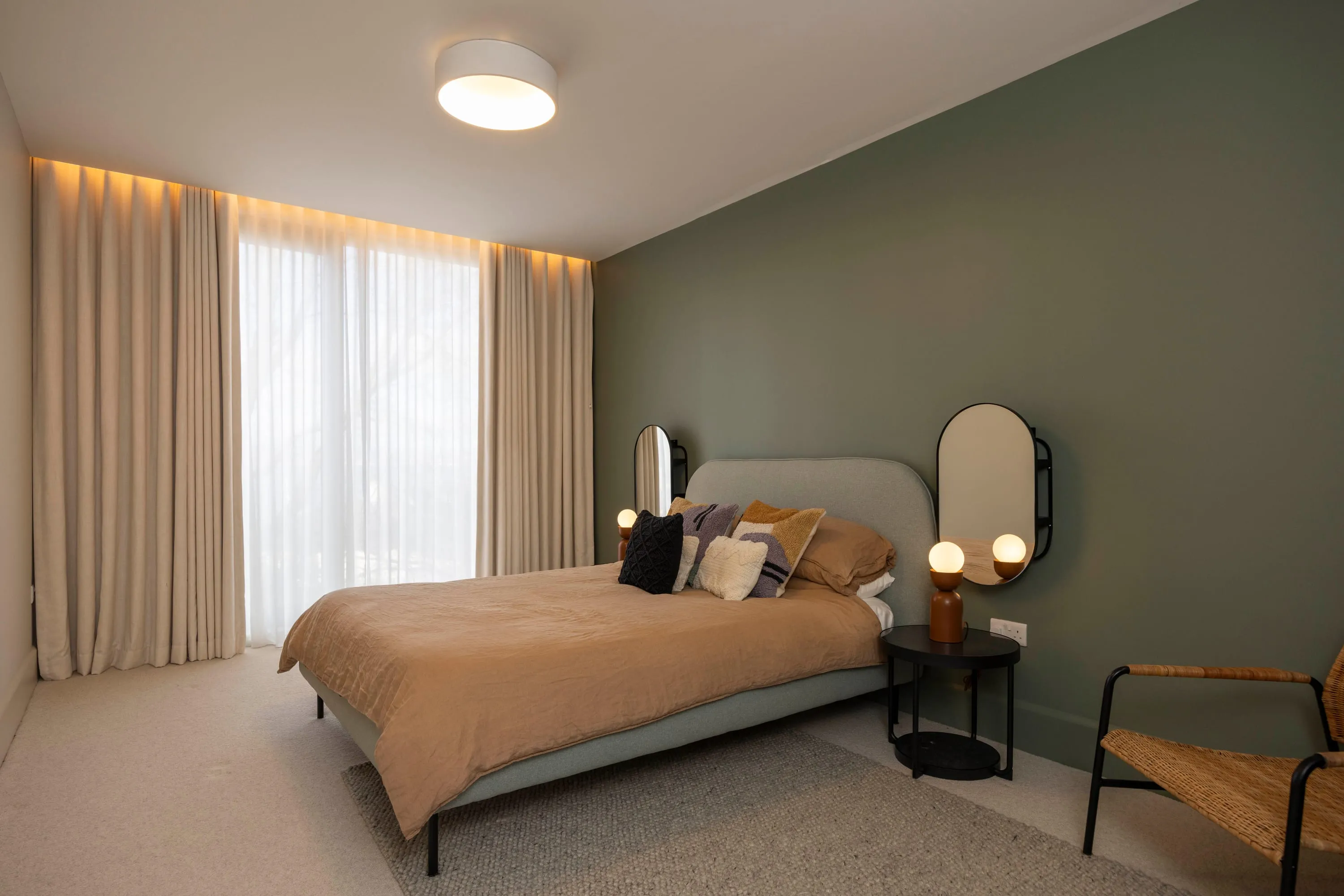 Bedroom two with sage green wall and rattan chair