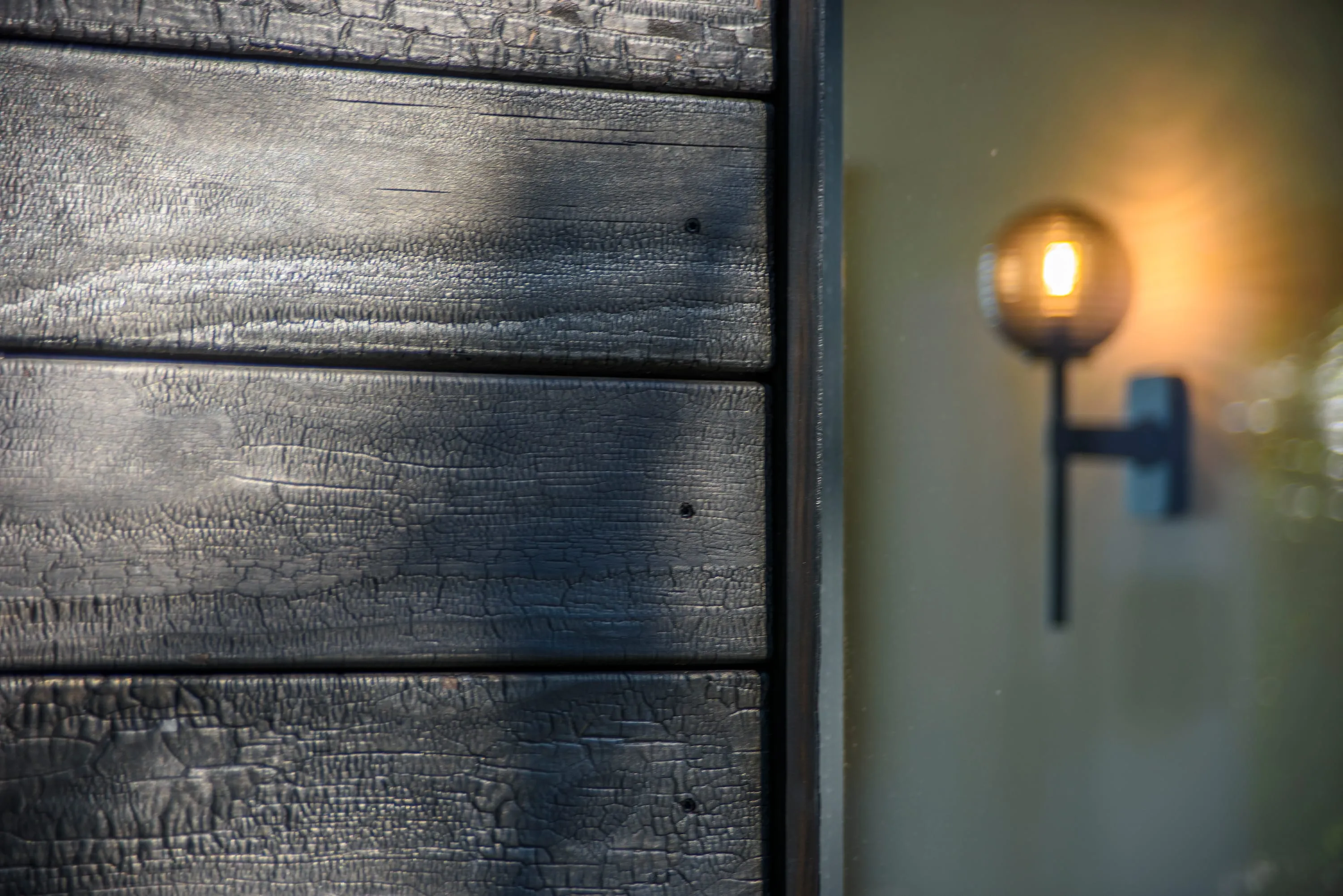 Exterior wall light against charred timber