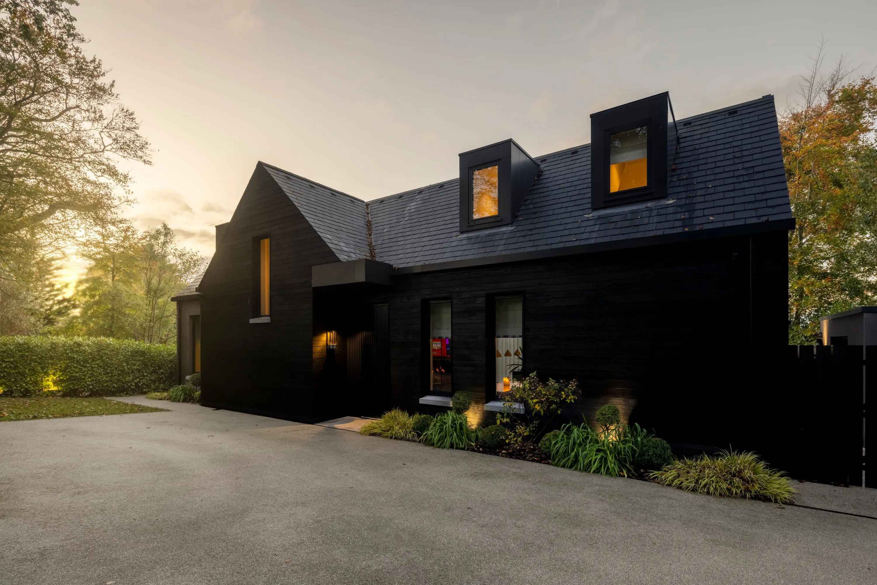 Front elevation of 26 Clanbrassil Road at dusk, scorched timber cladding, lit dormer windows and resin driveway