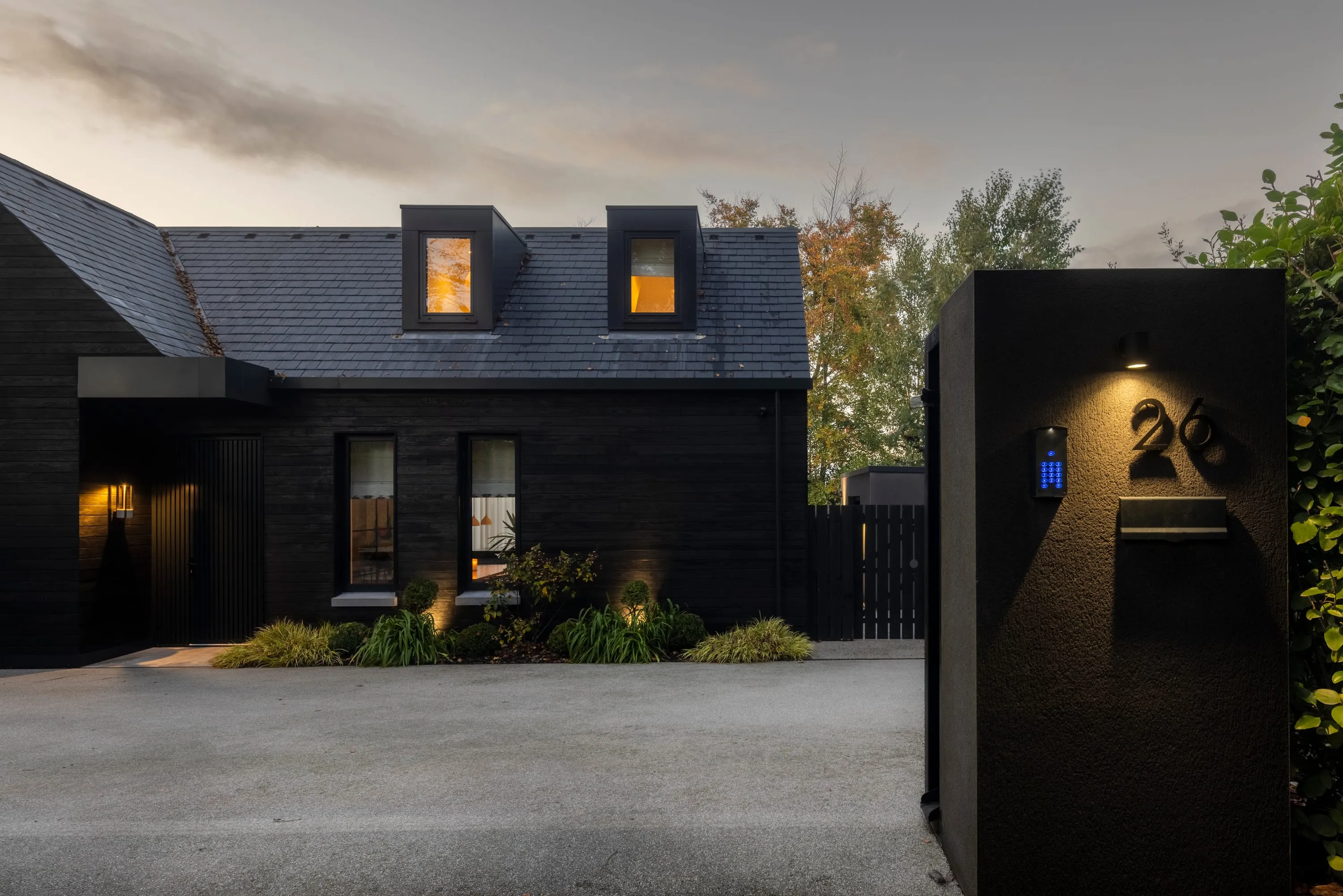 Dusk view across the driveway to the front door and lit windows