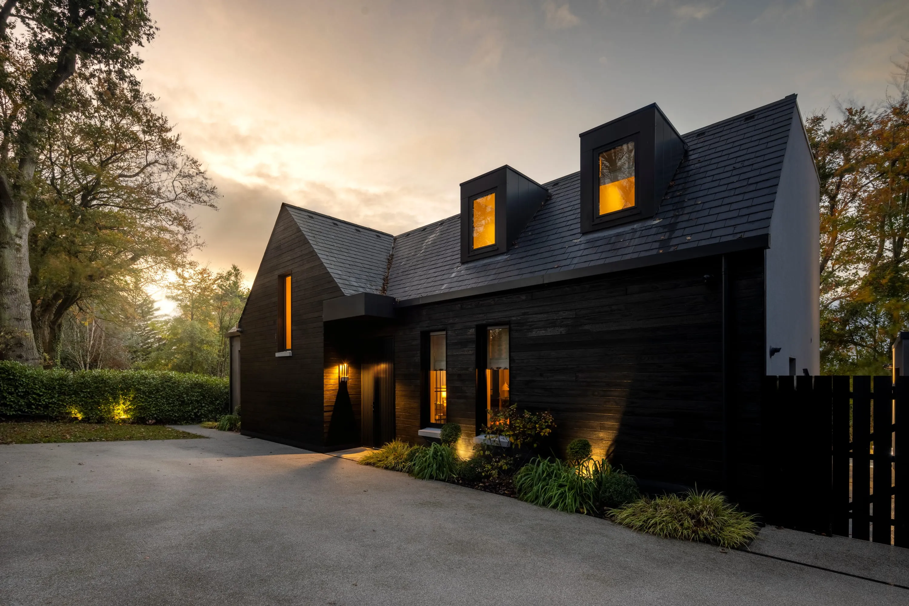 Wide dusk view of the house and driveway under mature trees