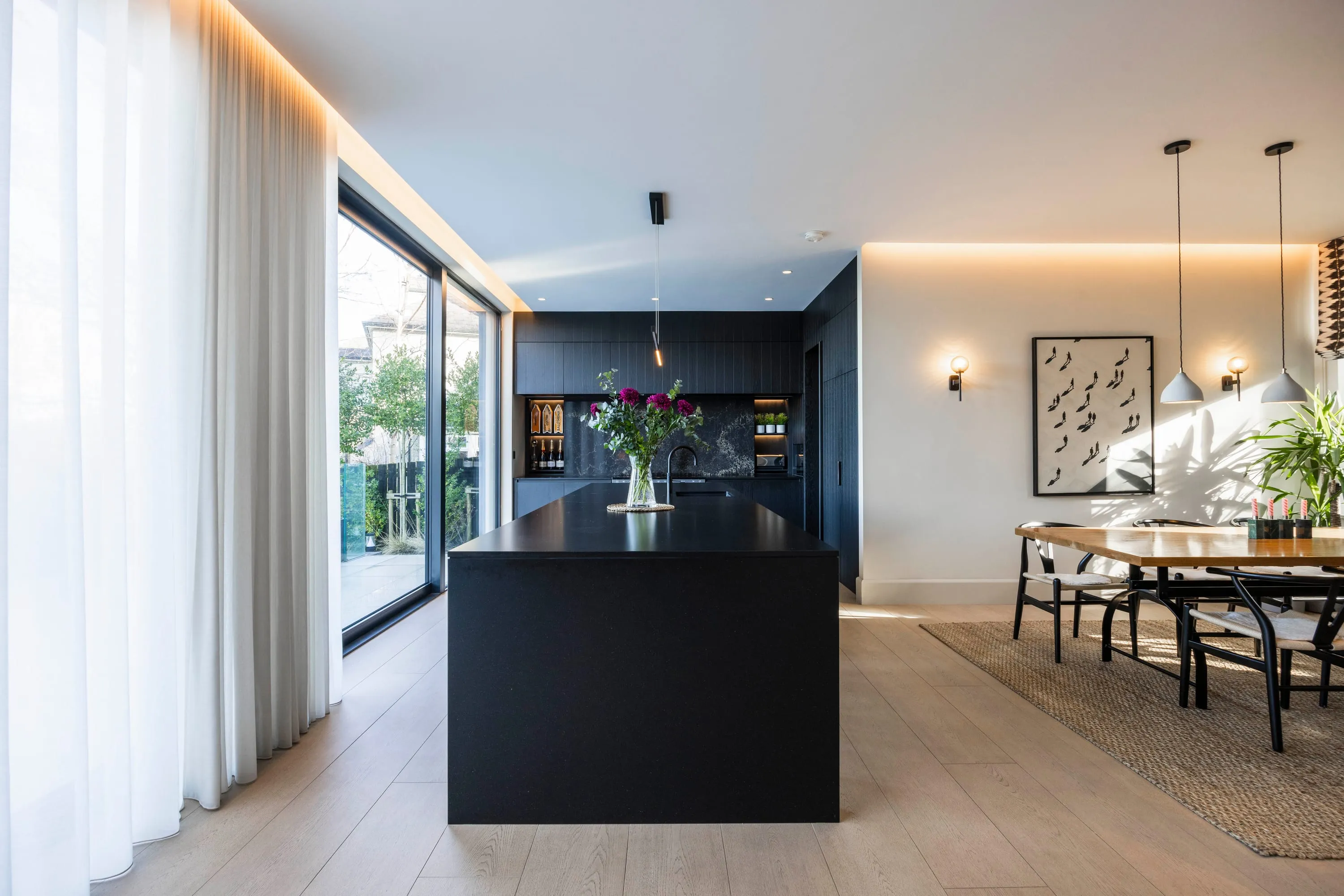 Open-plan kitchen with black island and dining table, sliding doors to the terrace